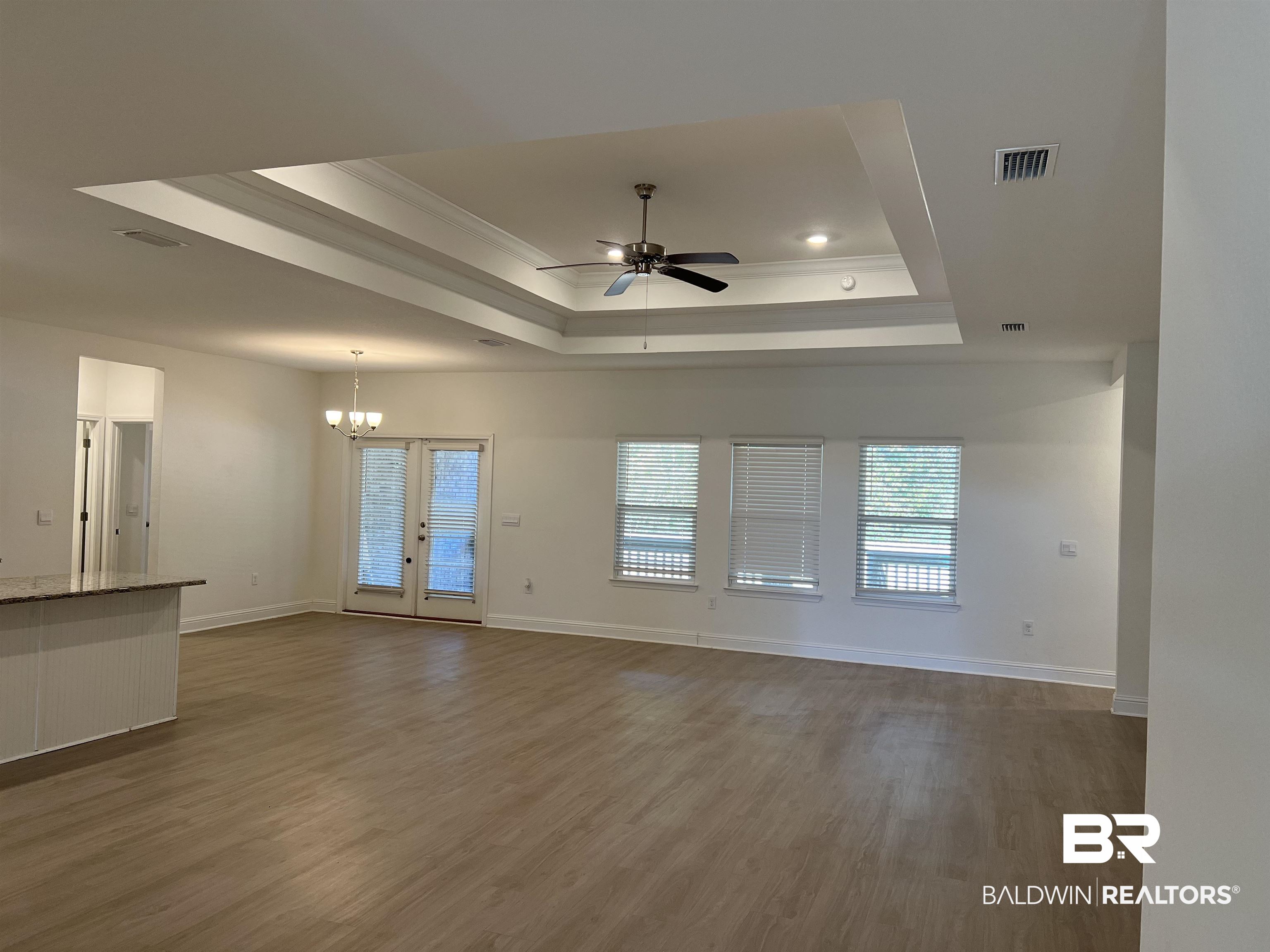 8855 Calverton Street Foley, AL 36535 - Photo 25 of 76 Unfurnished living room with french doors, ceiling fan with notable chandelier, crown molding, dark hardwood / wood-style floors, and a tray ceiling