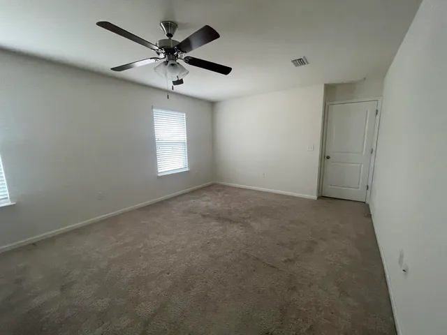 an empty room with a chandelier fan and windows