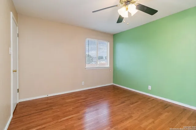 an empty room with wooden floor chandelier fan and windows