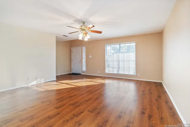 an empty room with wooden floor chandelier fan and windows