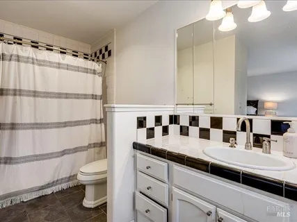 a bathroom with a granite countertop sink a toilet a mirror and shower