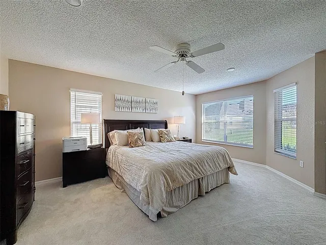 a spacious bedroom with a bed painting on wall and windows