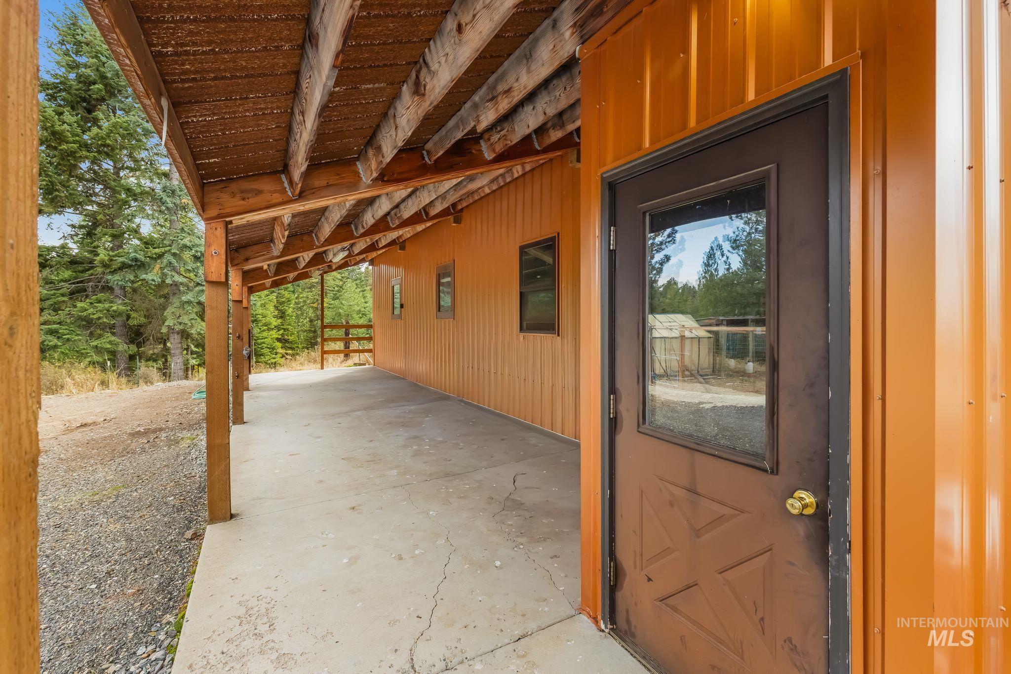 3989 East Mountain Road Anatone, WA 99401 - Photo 29 of 49 Covered concrete patio with exposed wooden beams, brown metal exterior siding, and a brown entry door with a glass insert