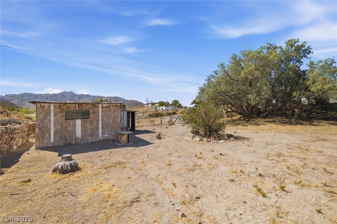 405 Main Street Beatty, NV 89003 - Photo 23 of 28 A rustic desert lot awaits development, with mountains in the distance and mature trees providing natural shade.