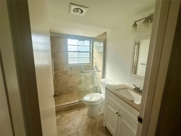 a bathroom with a granite countertop toilet a sink a mirror and a shower