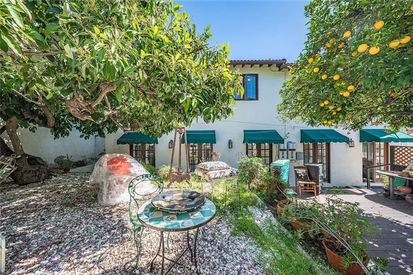 a backyard of a house with table and chairs potted plants and a large tree