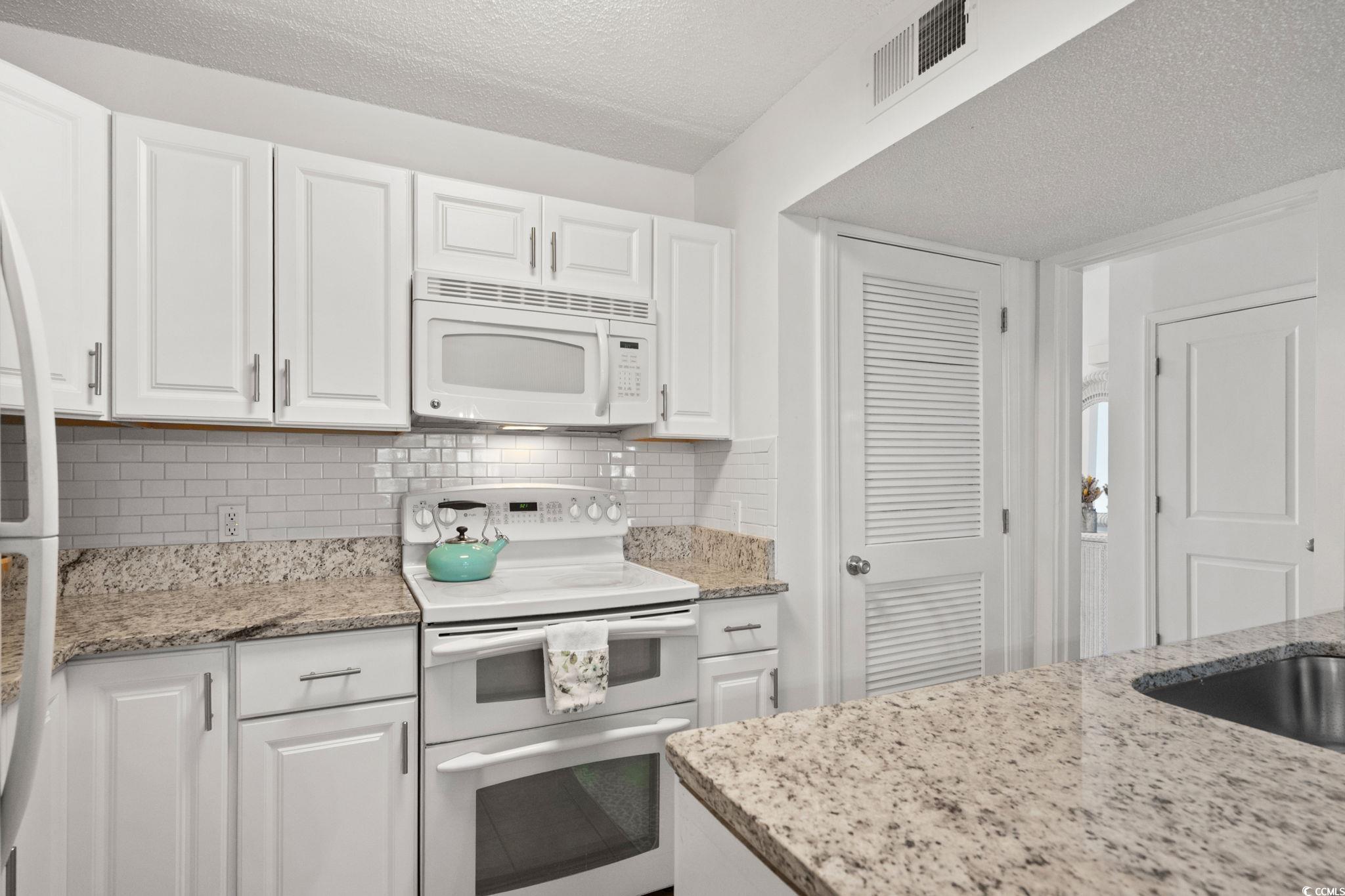500 Eagle Way, Unit 6 Little River, SC 29566 - Photo 11 of 38 Kitchen featuring white appliances, white cabinets, light stone counters, a textured ceiling, and backsplash