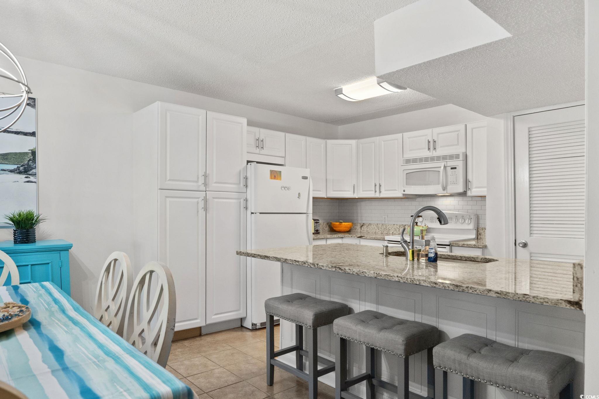 500 Eagle Way, Unit 6 Little River, SC 29566 - Photo 7 of 38 Kitchen with light stone countertops, white appliances, white cabinets, a kitchen breakfast bar, and a textured ceiling