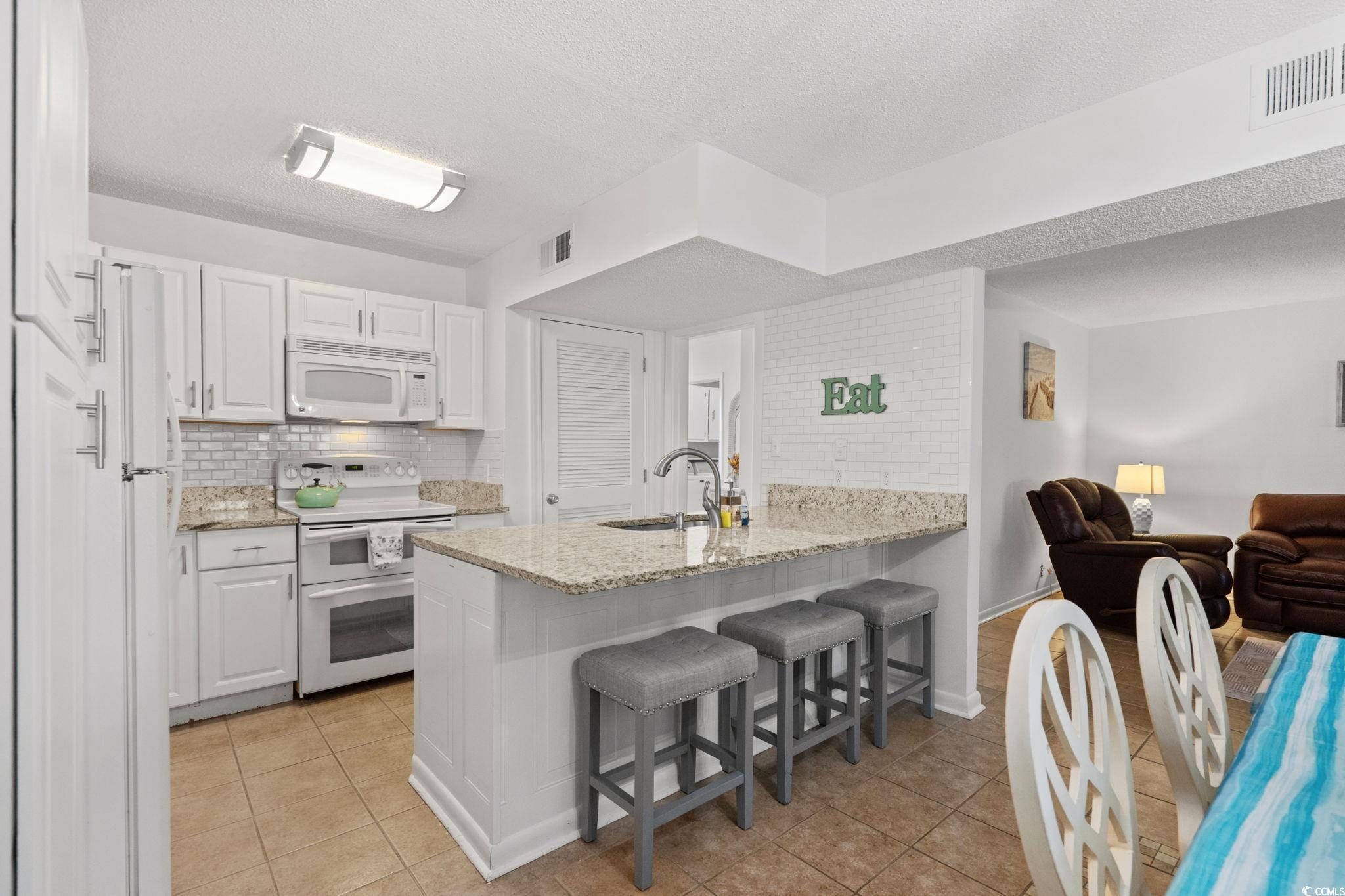 500 Eagle Way, Unit 6 Little River, SC 29566 - Photo 8 of 38 Kitchen featuring light stone countertops, white appliances, a breakfast bar area, a textured ceiling, and white cabinetry