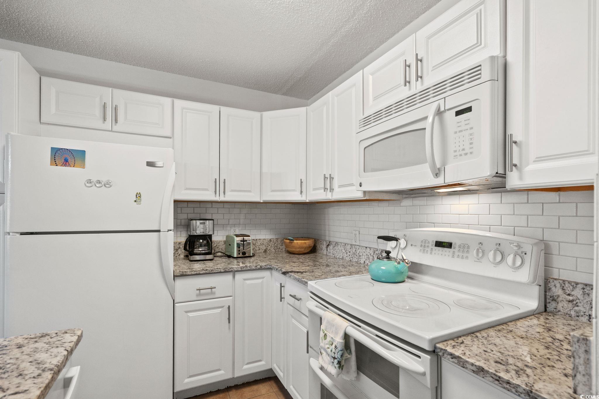 500 Eagle Way, Unit 6 Little River, SC 29566 - Photo 10 of 38 Kitchen featuring white appliances, light stone counters, white cabinetry, a textured ceiling, and decorative backsplash