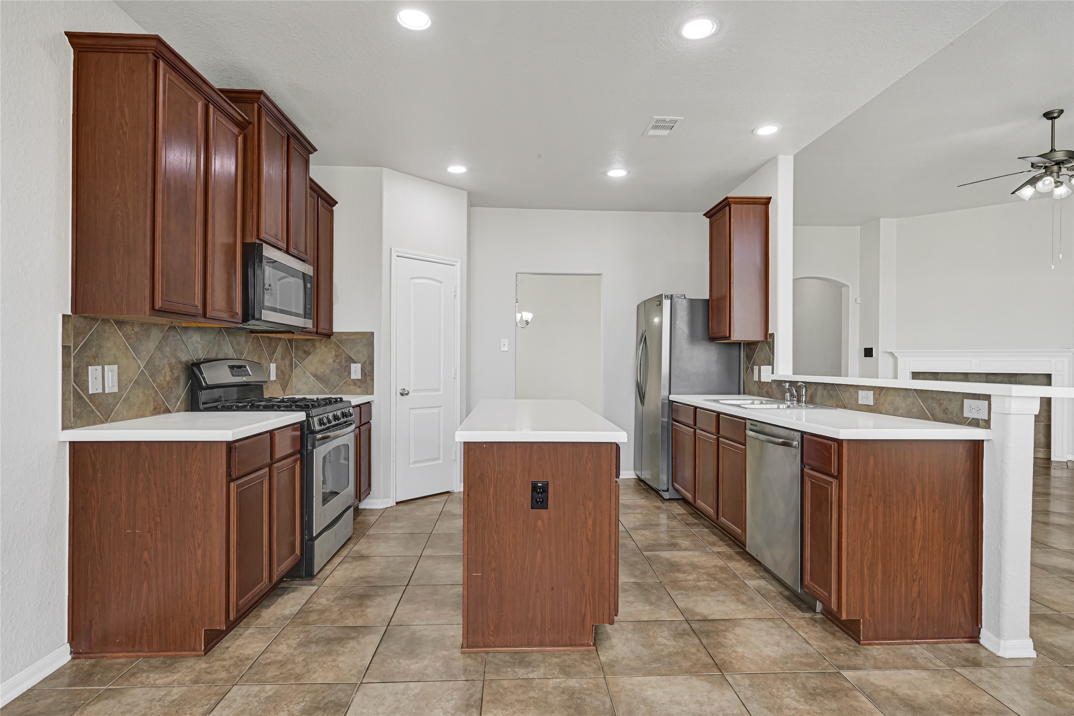 4702 Sedgewood Drive Rosenberg, TX 77471 - Photo 16 of 24 This kitchen features modern stainless steel appliances, ample wooden cabinetry, and a central island with a sleek countertop. The open layout seamlessly connects to the living area, enhanced by recessed lighting and neutral tile flooring, creating a bright and functional space.