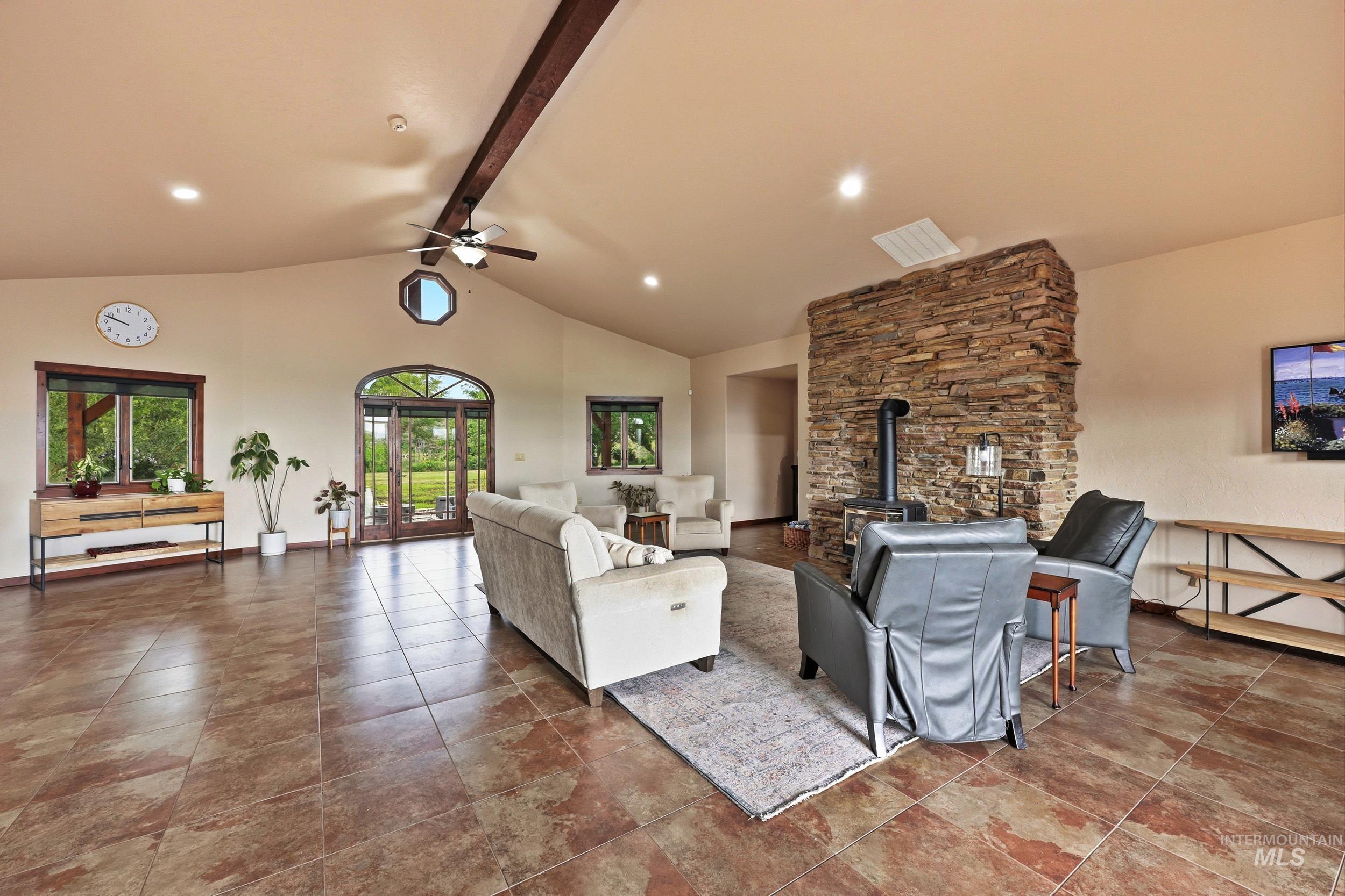 339 Airport Road Weiser, ID 83672 - Photo 9 of 49 Spacious living area featuring vaulted ceilings with exposed wood beams, a stone-clad wood-burning stove, and terracotta-toned tile flooring