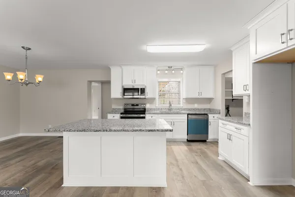 a kitchen with stainless steel appliances granite countertop a stove a sink dishwasher a refrigerator white cabinets and wooden floor