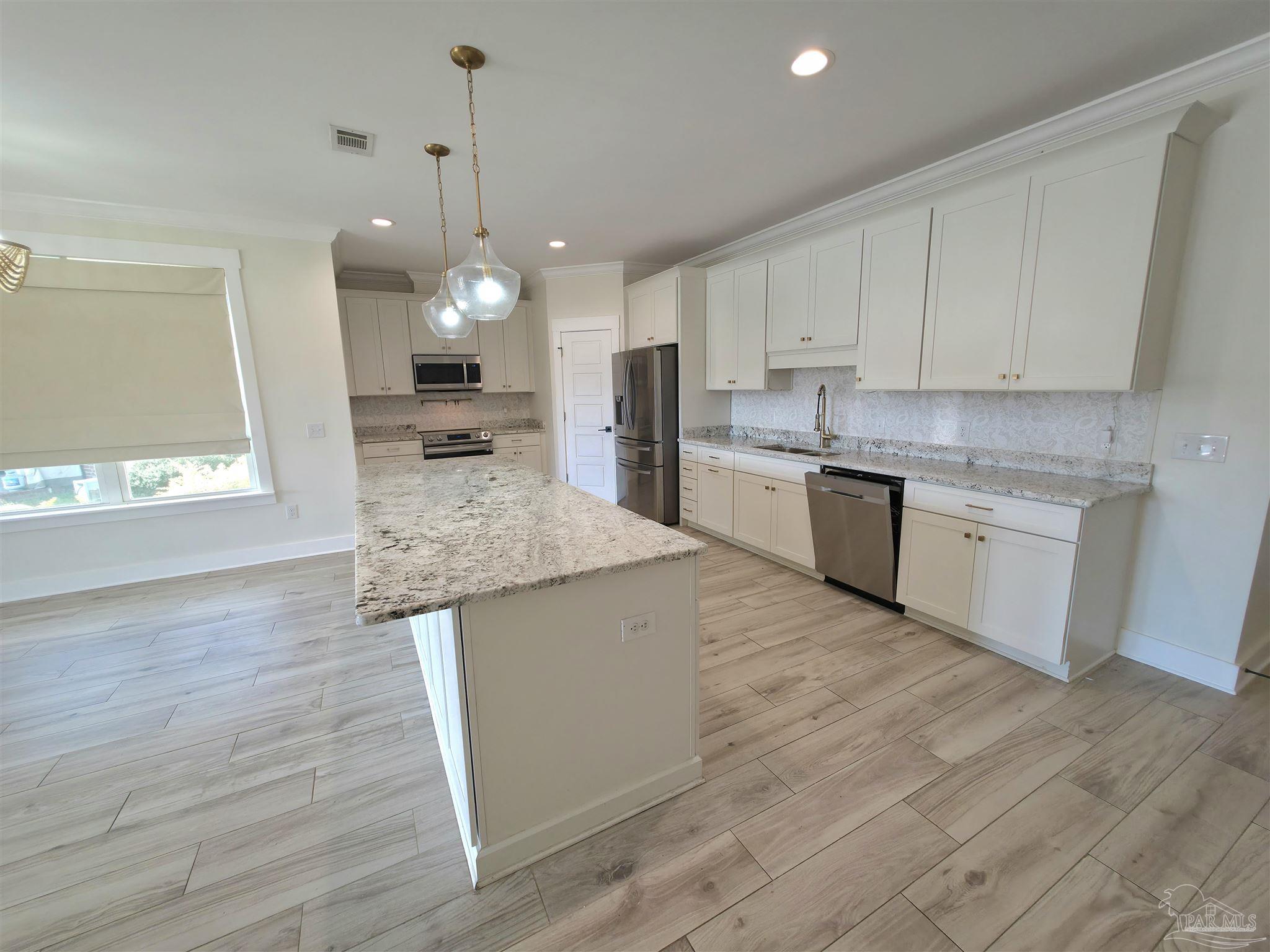 5642 Dunbar Circle Milton, FL 32583 - Photo 13 of 33 a kitchen with kitchen island granite countertop wooden floors and white cabinets