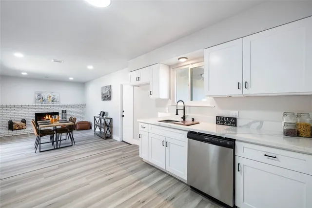 a kitchen with stainless steel appliances granite countertop a stove a sink dishwasher and white cabinets with wooden floor