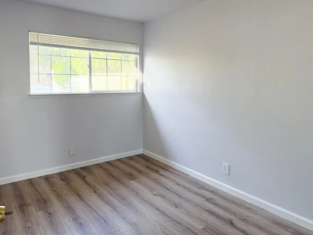 a view of an empty room with wooden floor and a window