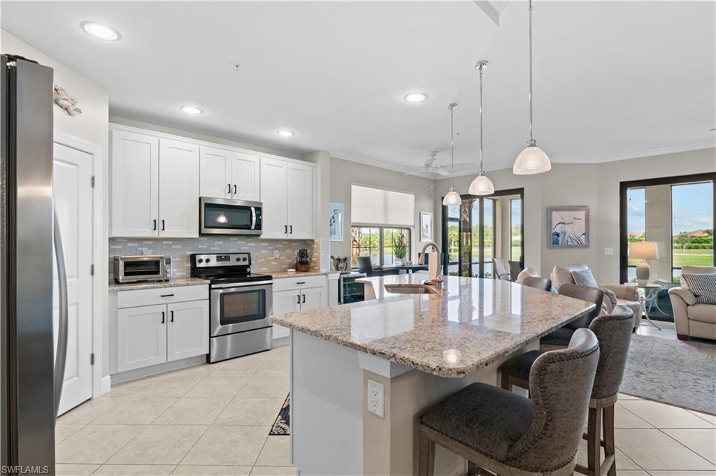10470 Casella Way, Unit 101 Fort Myers, FL 33913 - Photo 4 of 20 a kitchen with stainless steel appliances granite countertop a kitchen island hardwood floor sink stove dining table and chairs