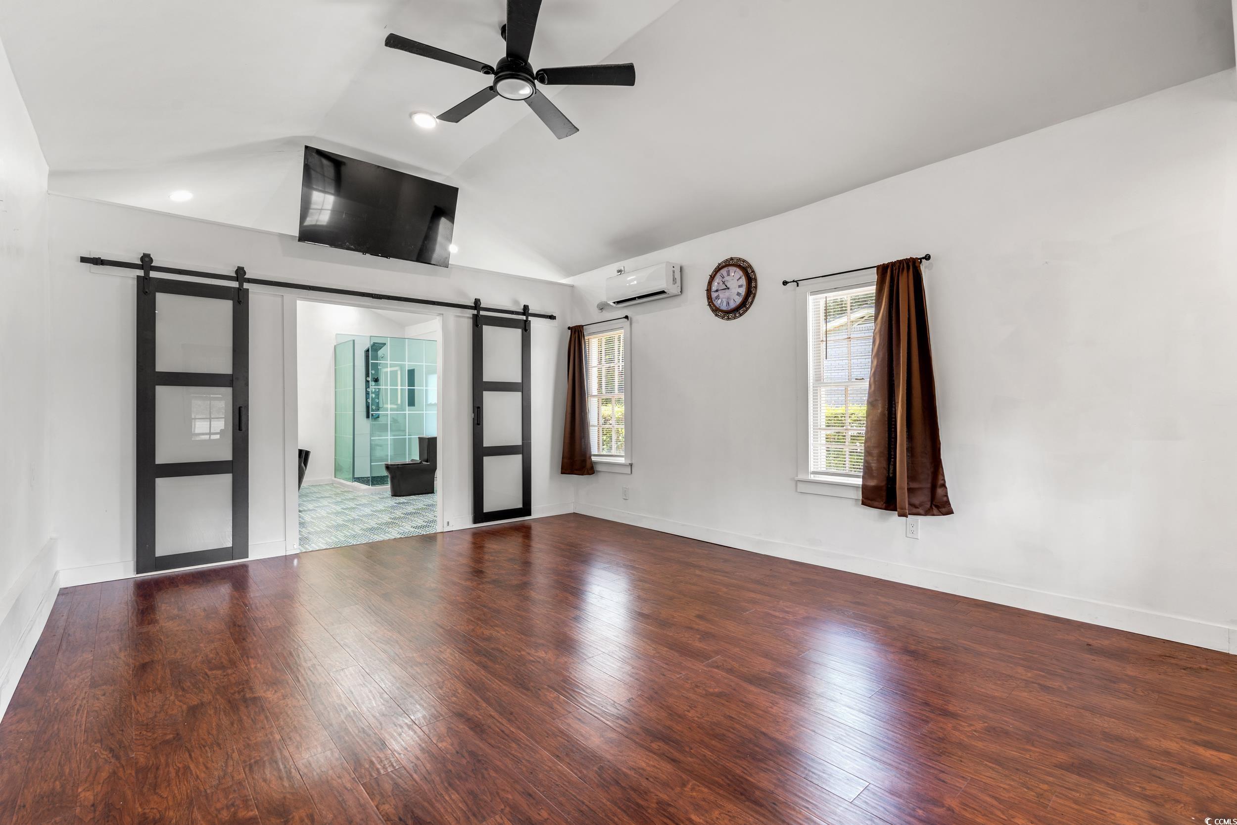 3974 North Fraser Street Georgetown, SC 29440 - Photo 16 of 36 Unfurnished living room featuring a barn door, lofted ceiling, a ceiling fan, wood finished floors, and a wall mounted air conditioner