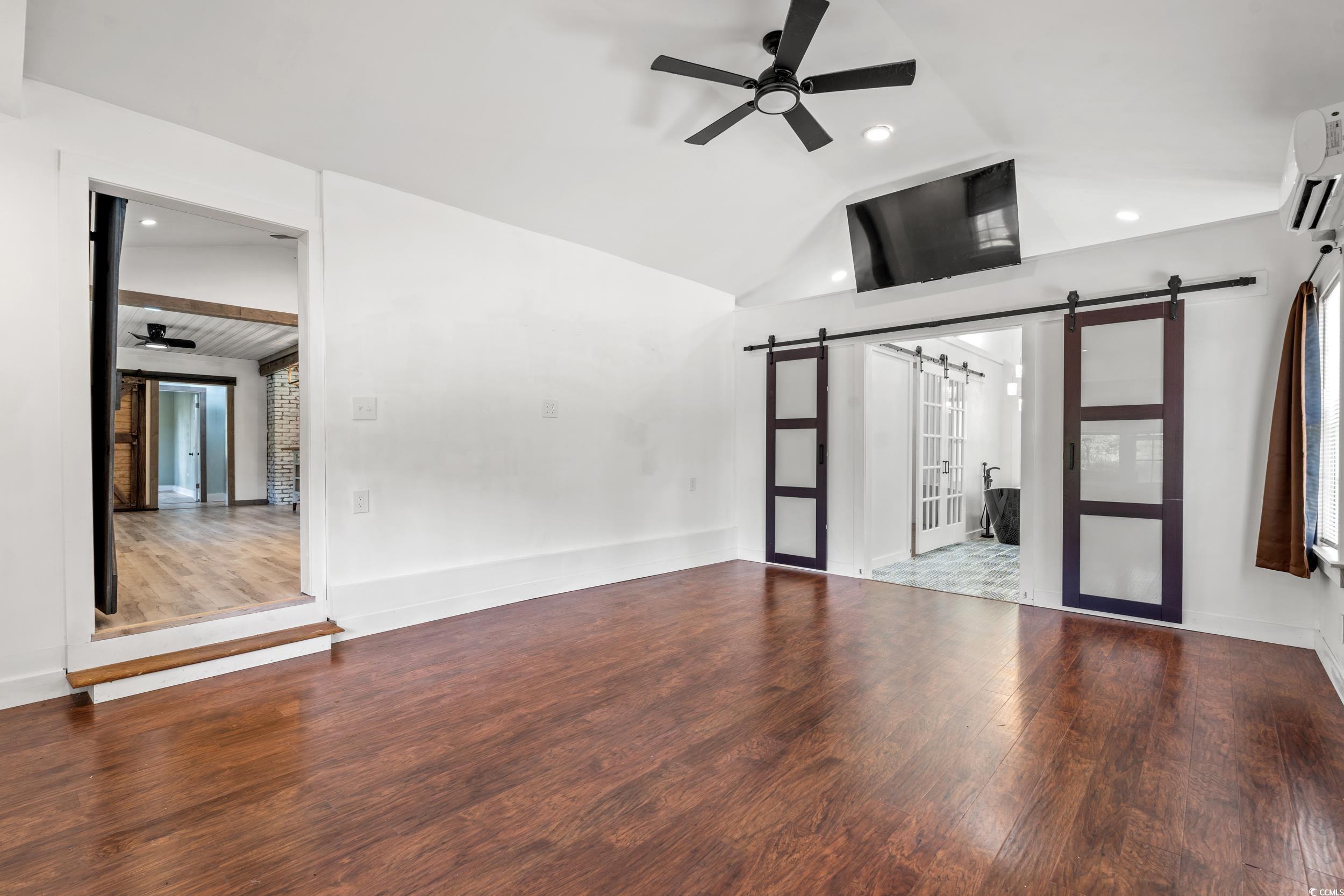 3974 North Fraser Street Georgetown, SC 29440 - Photo 17 of 36 Unfurnished living room featuring a barn door, a ceiling fan, vaulted ceiling, wood finished floors, and recessed lighting