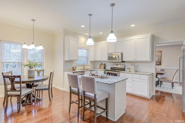 a kitchen with kitchen island a dining table chairs and white cabinets