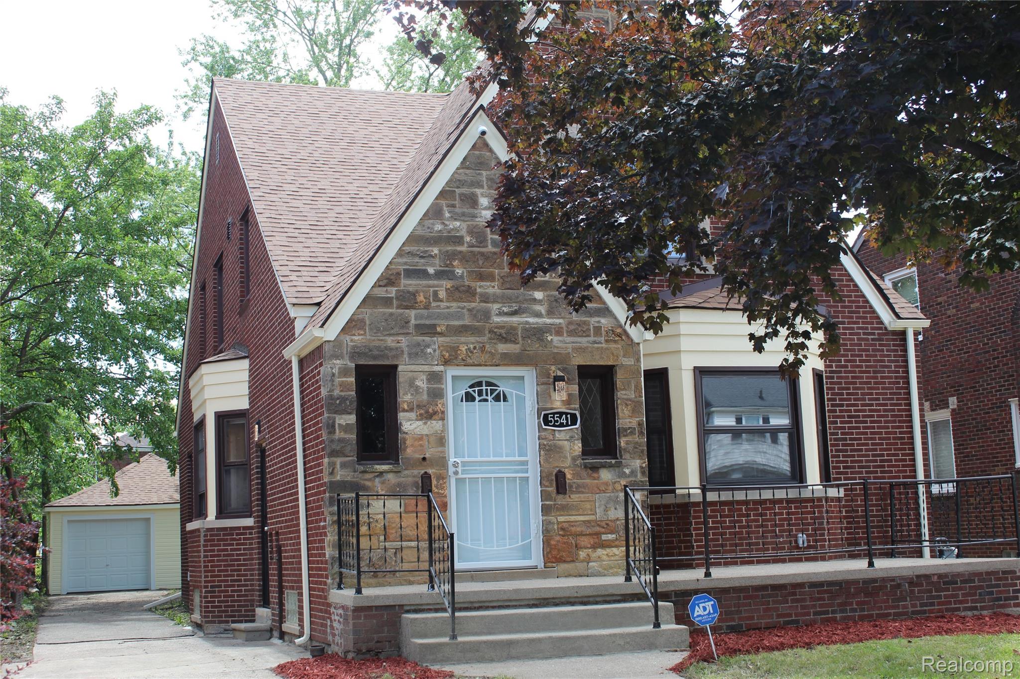 Brick and stone facade residence featuring a light blue front door, covered porch with black railings, and an attached two-car garage