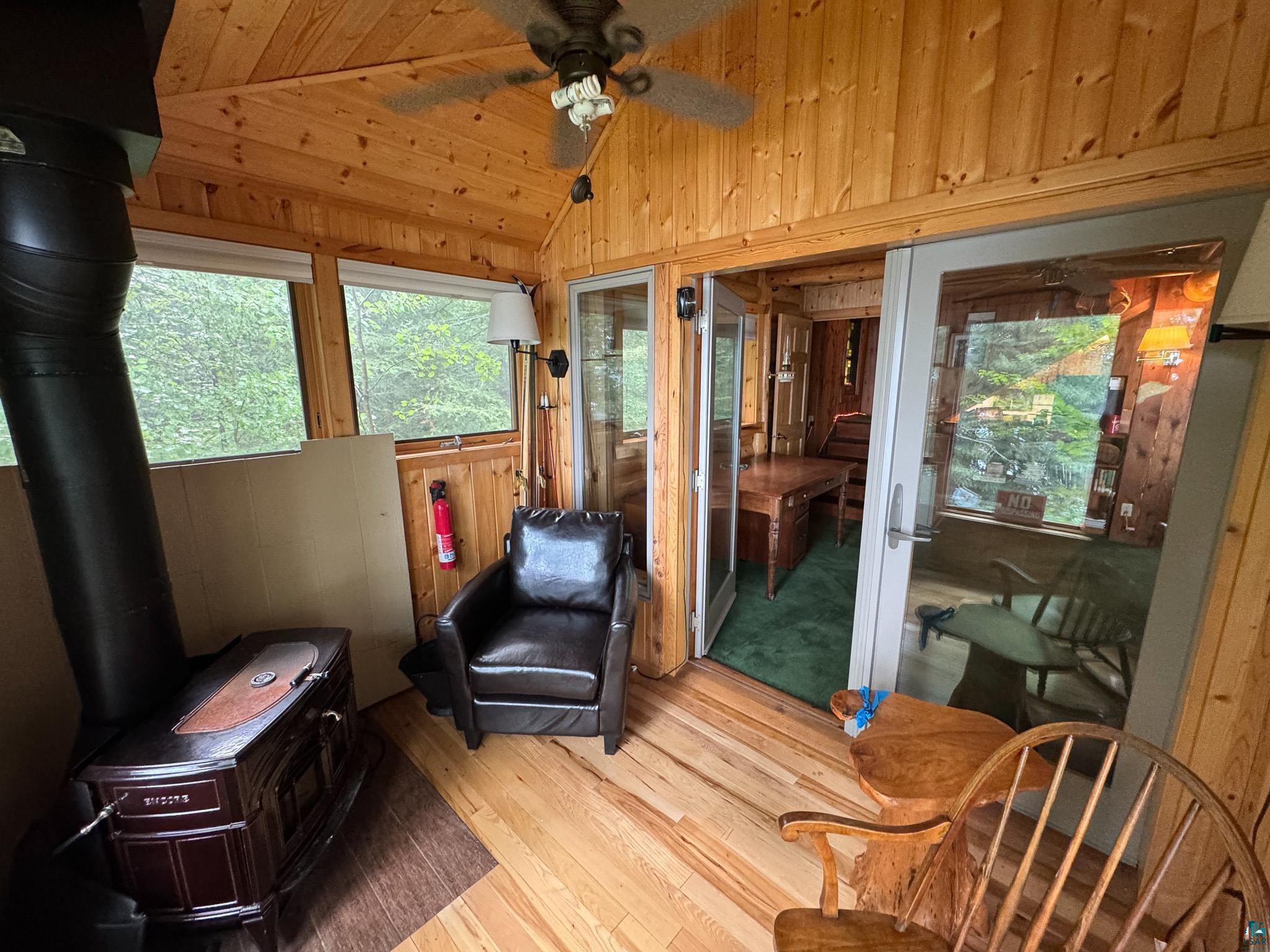 465 South Gunflint Lake Road Grand Marais, MN 55604 - Photo 30 of 46 Wood-paneled sunroom featuring natural wood-finish flooring, a cast iron stove, ceiling fan, and large windows