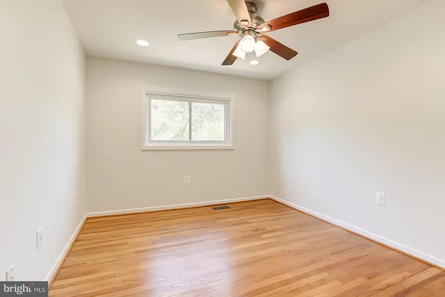 an empty room with wooden floor fan and windows