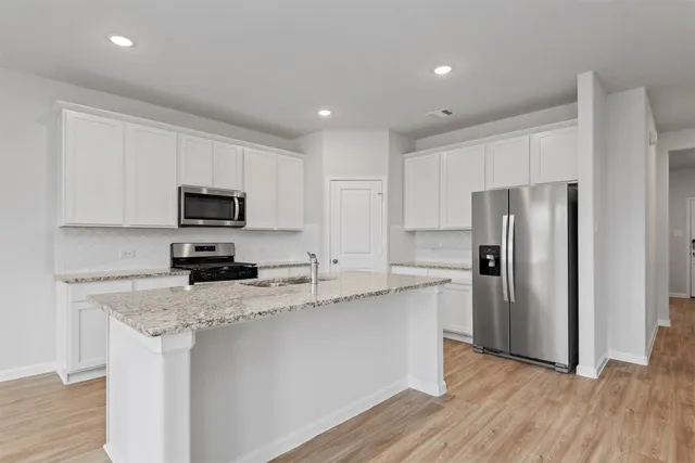 a kitchen with stainless steel appliances granite countertop a refrigerator a sink dishwasher a stove top oven a refrigerator with white cabinets and wooden floor
