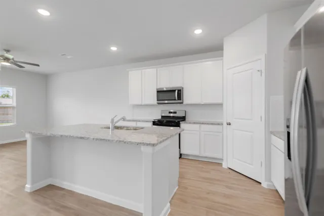 a kitchen with stainless steel appliances granite countertop a refrigerator a sink dishwasher a stove top oven a refrigerator and white cabinets with wooden floor