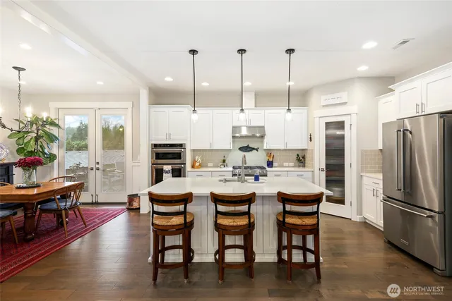 a kitchen with stainless steel appliances kitchen island granite countertop a stove a refrigerator a dining table and chairs with wooden floor