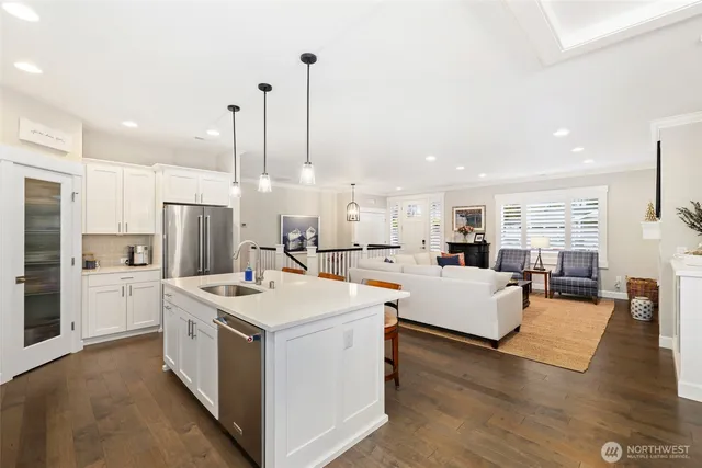a open kitchen with stainless steel appliances kitchen island granite countertop a stove top oven a refrigerator a sink and white cabinets with wooden floor