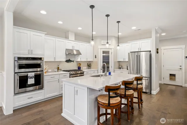 a kitchen with stainless steel appliances kitchen island granite countertop a stove a sink a refrigerator and chairs with wooden floor