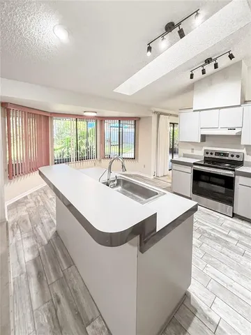 a large white room with kitchen island a stove a sink dishwasher and wooden cabinets