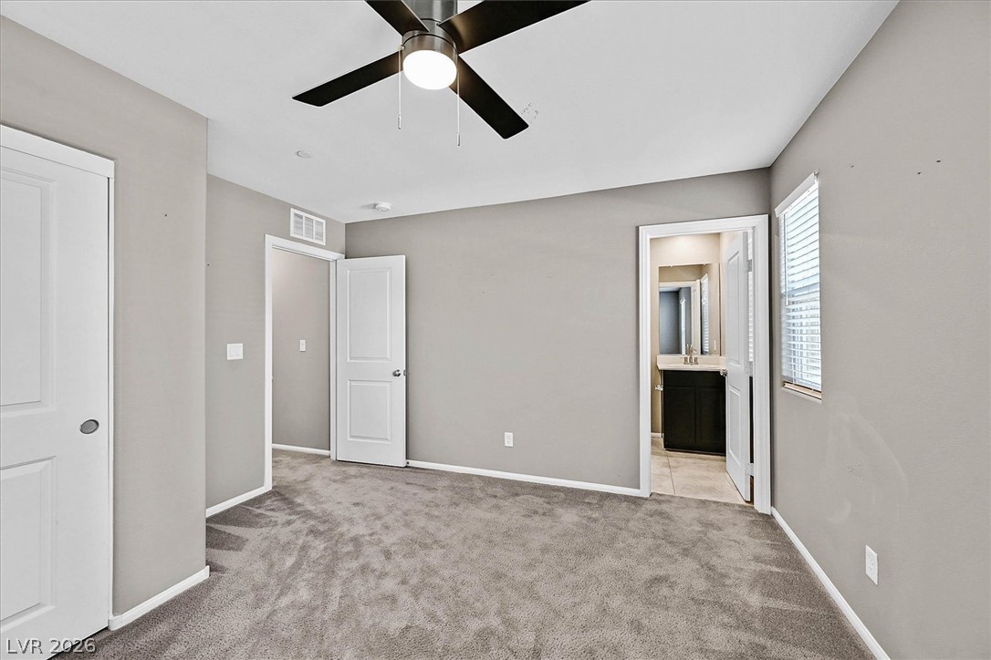 2823 Turnstone Ridge Street Henderson, NV 89044 - Photo 15 of 25 A comfortable primary bedroom with soft carpeting and a ceiling fan, offering a private entrance to an en-suite bathroom.