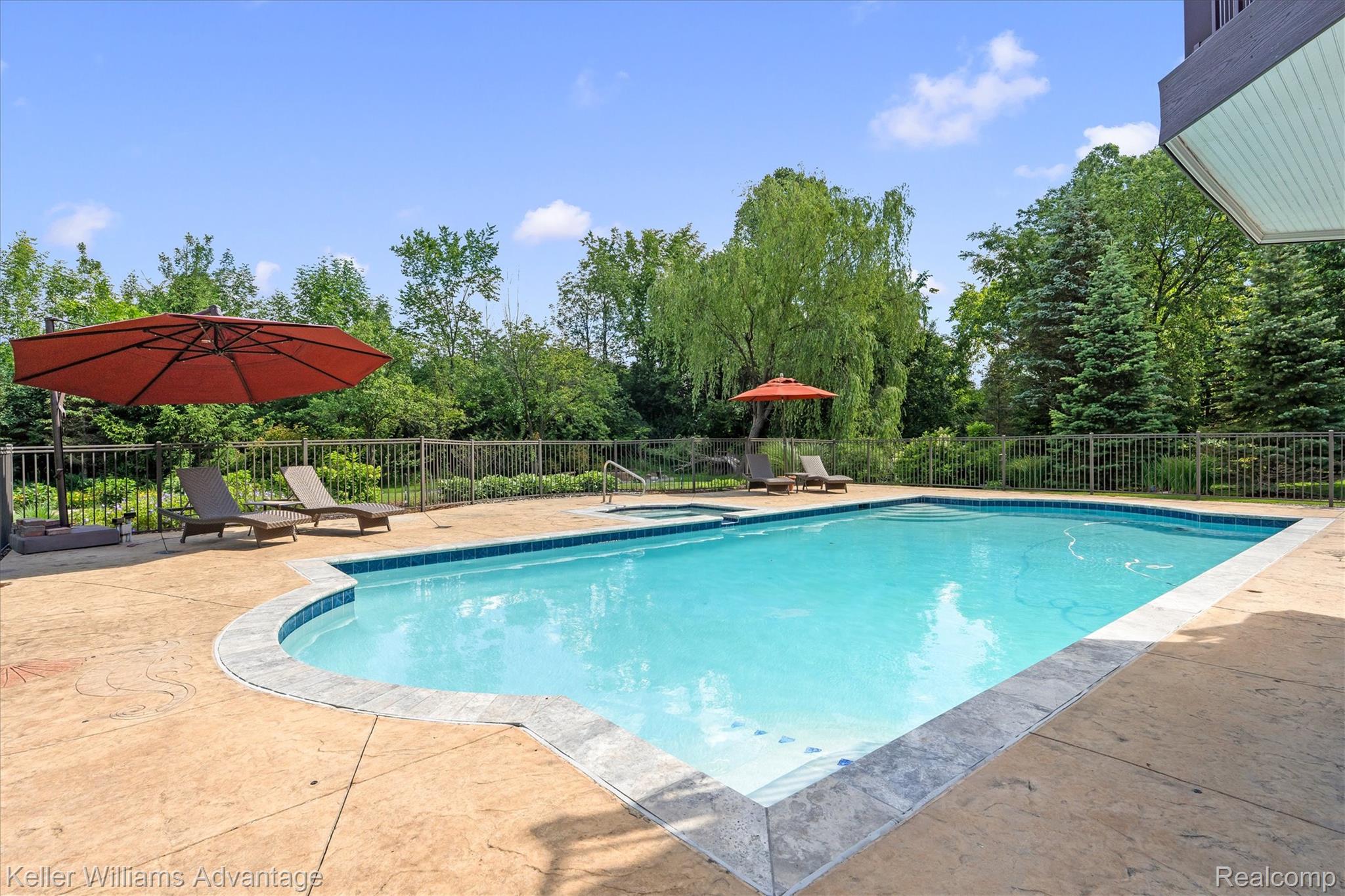 22878 Tree Top Court South Lyon, MI 48178 - Photo 51 of 75 In-ground swimming pool featuring a curved design, integrated spa, and concrete decking