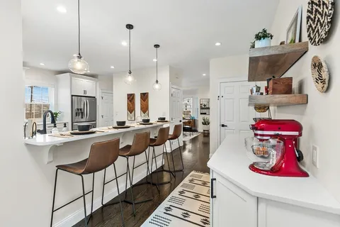 a kitchen with stainless steel appliances kitchen island granite countertop a dining table chairs sink and white cabinets