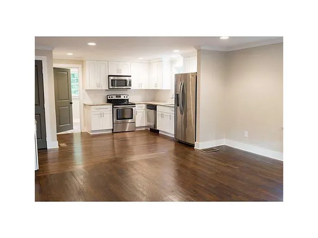 a room with stainless steel appliances kitchen island granite countertop a refrigerator a stove and a microwave with wooden floor