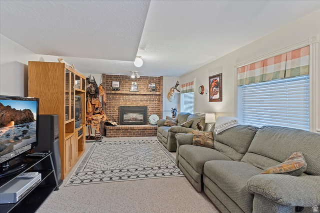 5321 South 3100th Street West Roy, UT 84067 - Photo 27 of 64 Spacious living area featuring a prominent brick fireplace with a dark metal insert, carpet flooring, multiple windows with blinds, and recessed ceiling lighting