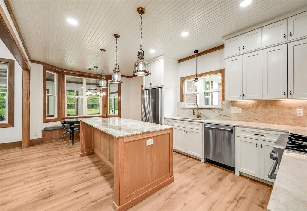 1037 Harrison Road Denison, TX 75021 - Photo 15 of 39 Kitchen featuring a large central island with a light-toned countertop, wood-finish flooring, white upper and lower cabinetry, stainless steel appliances, and a shiplap ceiling