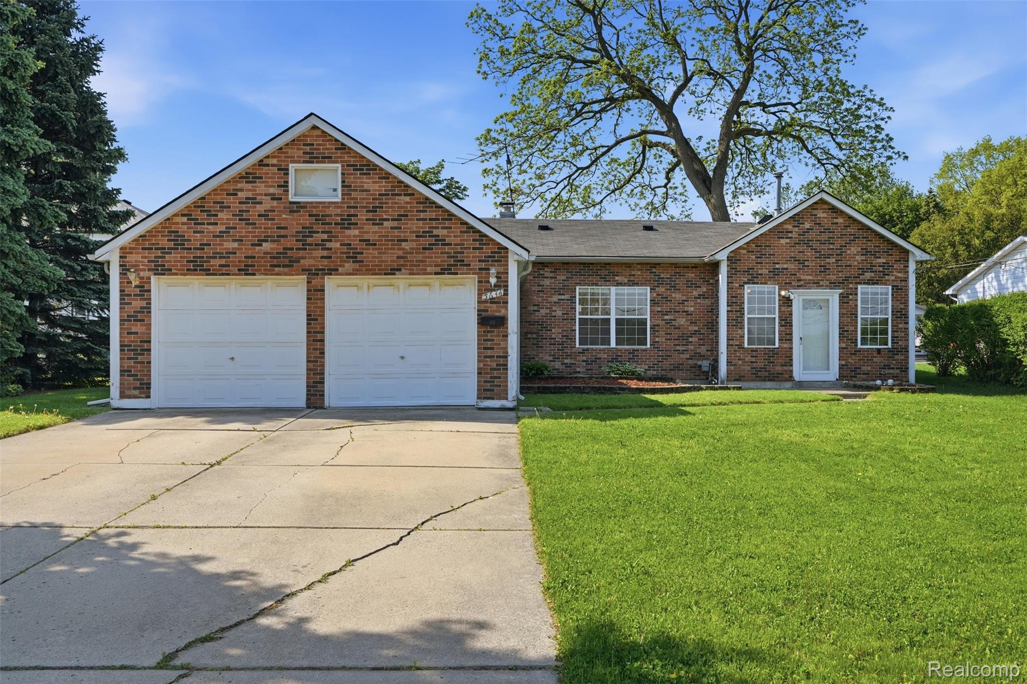 5634 Chicago Road Warren, MI 48092 - Photo 2 of 36 Brick exterior residence featuring an attached two-car garage, white garage doors, a front lawn, and a paved driveway