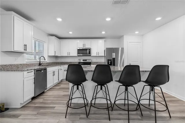 a kitchen with stainless steel appliances granite countertop a table chairs sink and cabinets