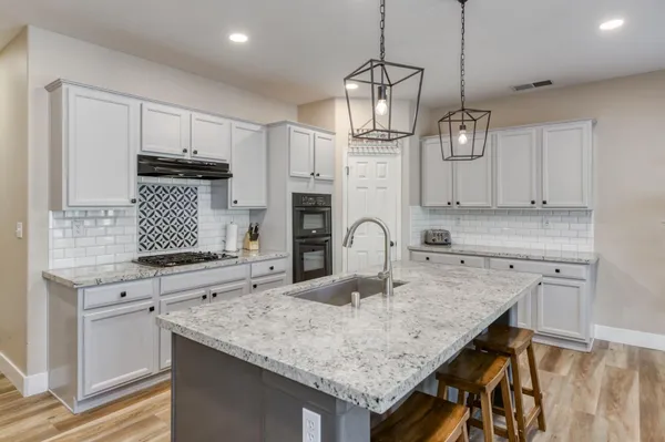a kitchen with stainless steel appliances kitchen island granite countertop a wooden floor and white cabinets