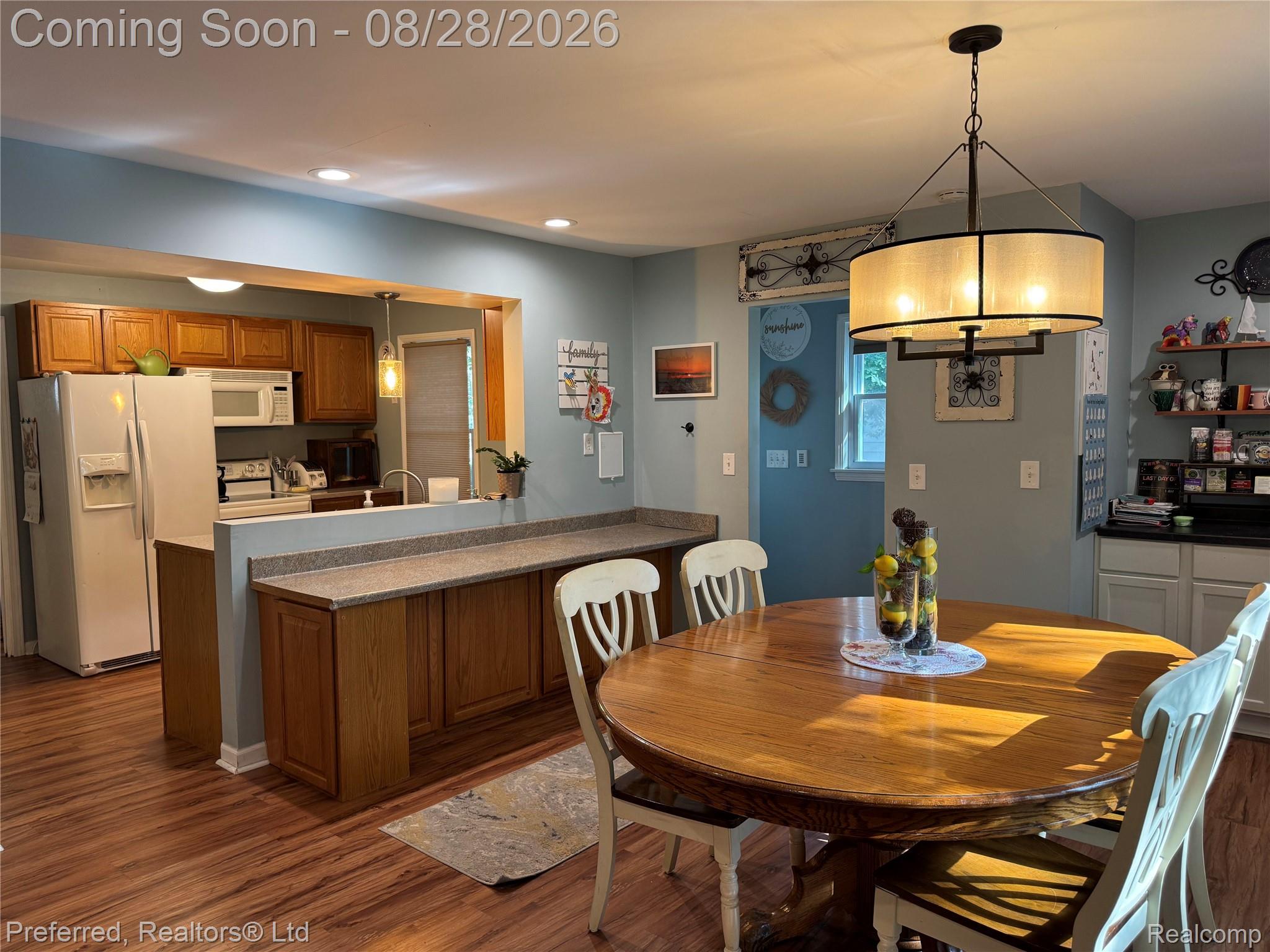 10362 Quirk Road Belleville, MI 48111 - Photo 11 of 41 Wood-finish flooring, recessed lighting, and a drum pendant light fixture illuminate this open-concept kitchen and dining area with wood cabinetry and a pass-through counter