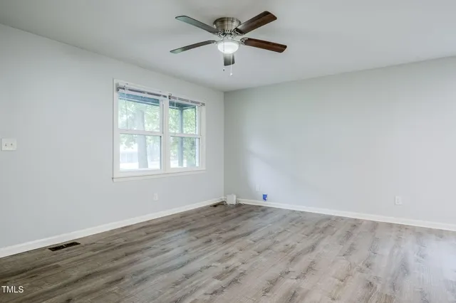 an empty room with wooden floor chandelier fan and windows