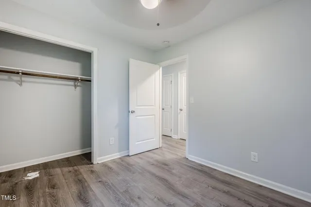 an empty room with a chandelier fan and wooden floor