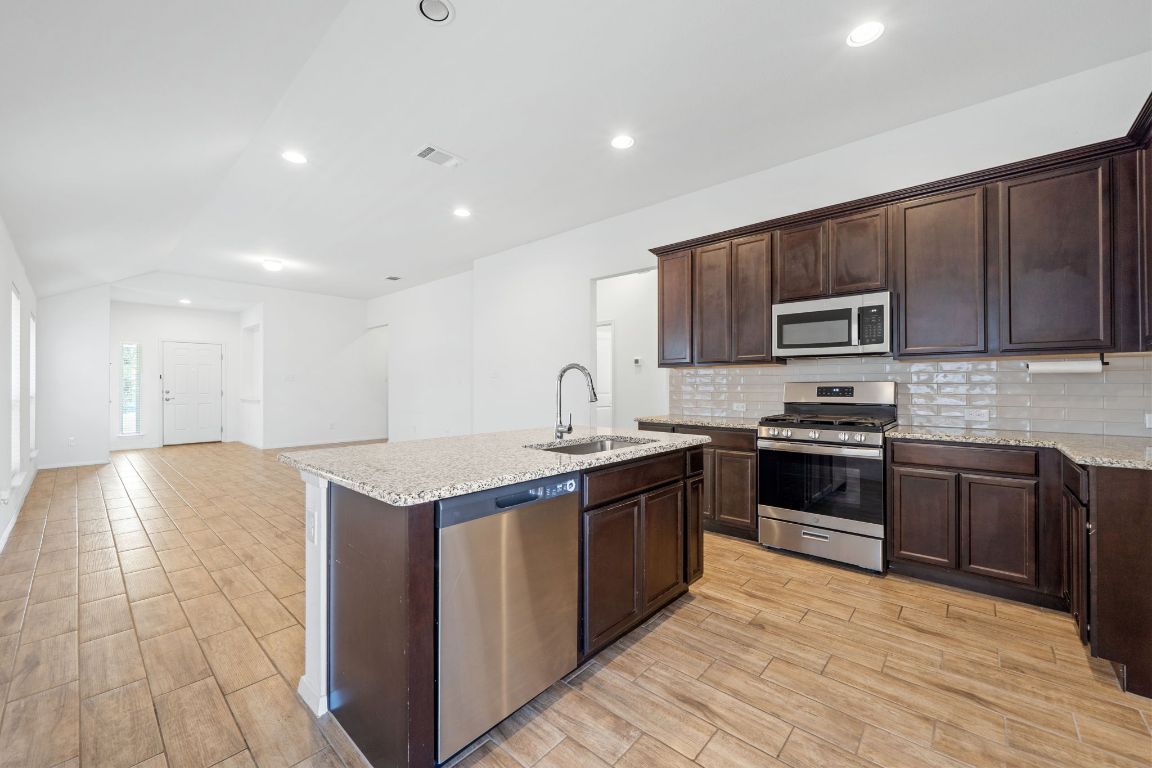 219 Trailside Lane Bastrop, TX 78602 - Photo 4 of 19 a large kitchen with stainless steel appliances granite countertop a stove a sink and a microwave