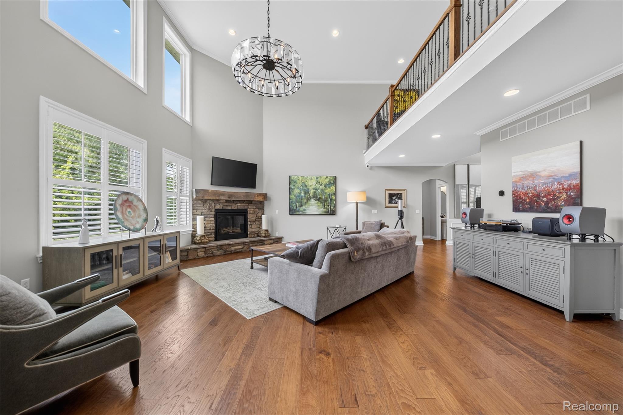 2531 Walnut View Drive Howell, MI 48855 - Photo 10 of 34 Two-story living area featuring wood-finish flooring, a stone-surround fireplace with a wooden mantel, and a multi-tiered crystal chandelier