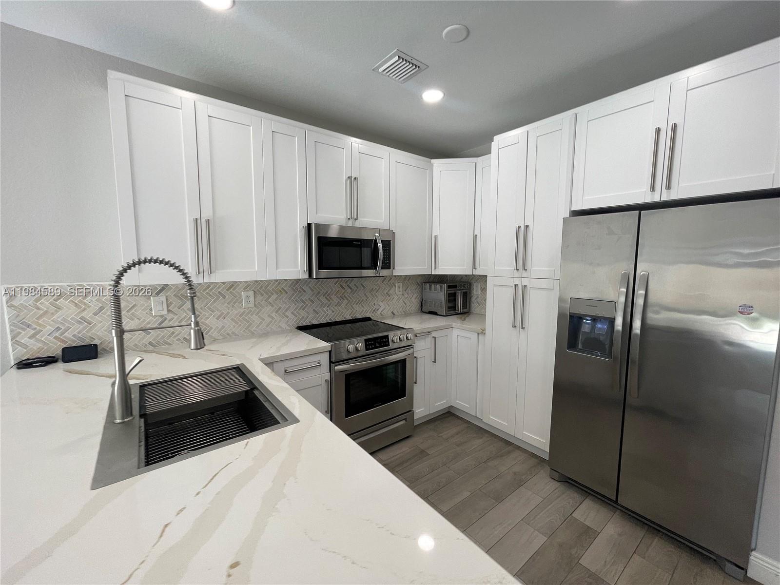 8900 Southwest 226th Terrace Cutler Bay, FL 33190 - Photo 7 of 40 a kitchen with stainless steel appliances a refrigerator sink and white cabinets