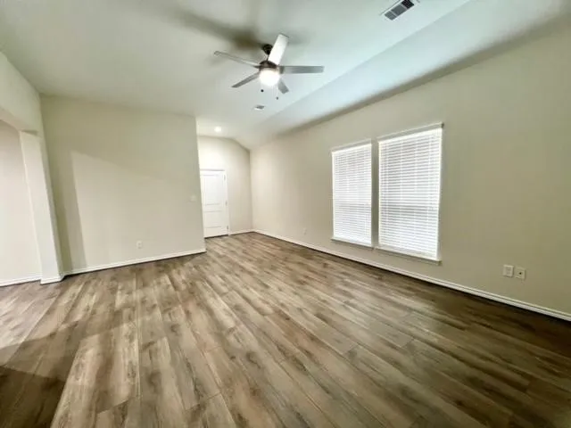 an empty room with wooden floor chandelier fan and windows