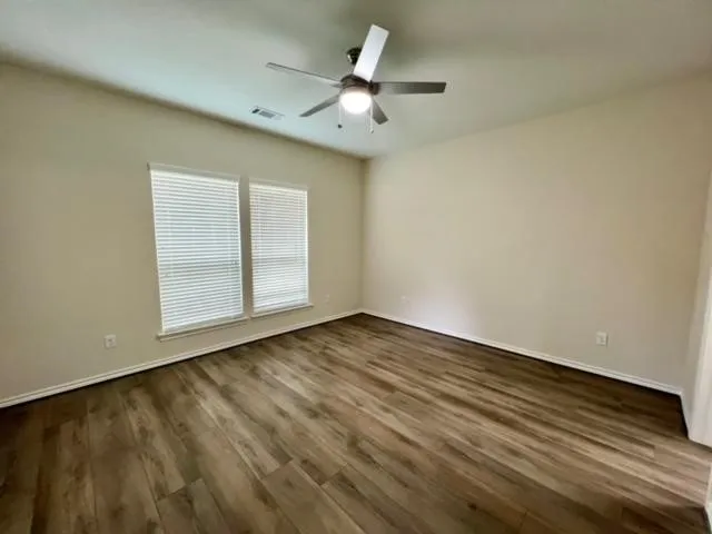 an empty room with wooden floor fan and windows